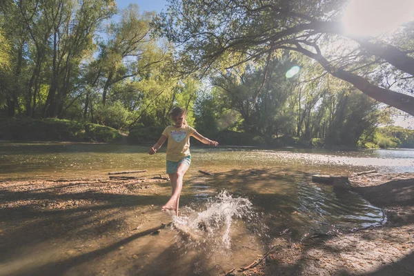 active girl having fun in shallow river in golden hour time in romantic green park
