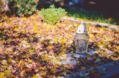 Güneşli bir öğleden sonra, renkli sonbahar atmosferiyle mezarda mum yakmak.