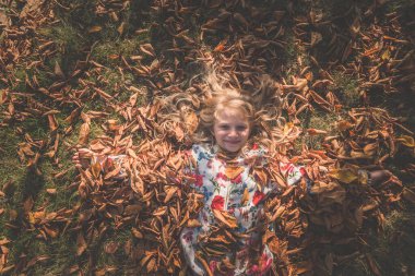 Kuşbakışı bakış açısından, güneşli bir günde yaprakların arasında uzanan güzel sarışın kıza.