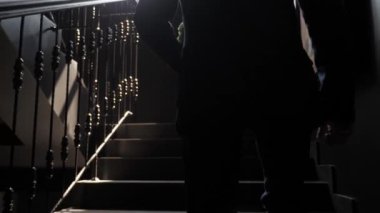 Bir adam elinde bir buket ile ahşap bir merdiven boyunca yürür. Büyük pencere. Pencereden güneş ışığı. Damat geline gider..