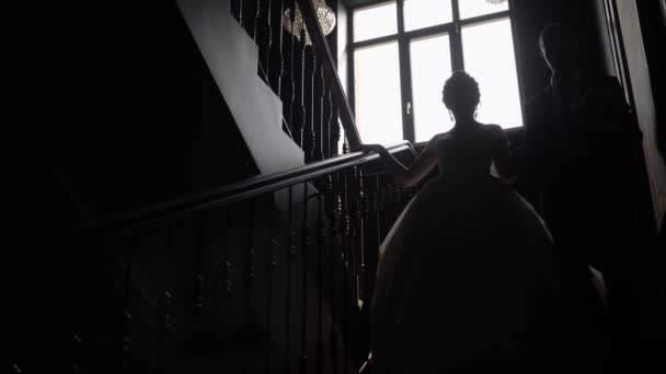新郎新婦は手で一緒に階段を下りる 大きな窓を背景に階段を歩く男女 — ストック動画