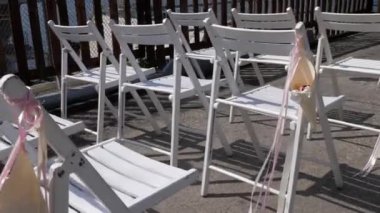 Ahşap katlanır sandalye sıraları nehrin kıyısında duruyor. Sandalyeler rüzgar ve çiçek yaprakları gelişen kurdeleler ile dekore edilmiştir. Düğün törenine hazırlanıyorum. 3 eksenli motorlu gimbal stabilizatör ile filme.