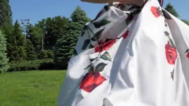 Bir erkek ve bir kadın eliyle yeşil çayırda koşarlar, kırmızı gül çizimleri olan uzun beyaz etekli bir kadın. Bir kadın etek tutar, bir erkek ona yardım eder. 3 eksenli motorlu gimbal stabilizatör ile çekim.