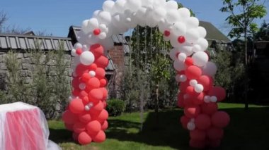 Kırmızı ve beyaz balonlardan yapılmış düğün kemeri, ziyaret töreni, yeşil çim.