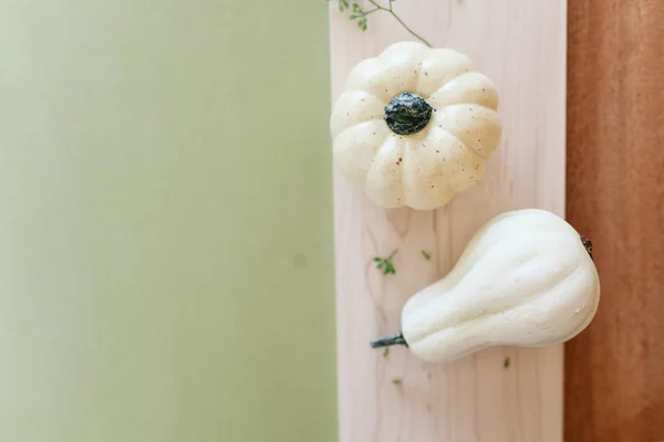 Small cream pumpkins on a wooden tray and  sage green background with dry plants and eucalyptus leaves decoration. Flat lay. Side view.