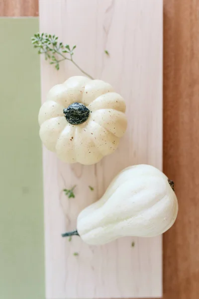 Small cream pumpkins on a wooden tray and  sage green background with dry plants and eucalyptus leaves decoration. Flat lay. Side view.