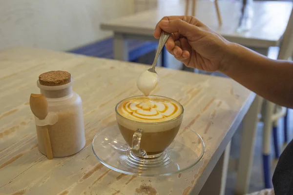 スプーンを持つ手はテーブルの上のコーヒー カフェラテのコーヒー Cup 泡を置く — ストック写真