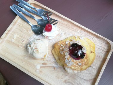 Vanilyalı krep, yaban mersini soslu badem ve ahşap tabakta şeker kreması.