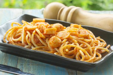 Masada siyah tabakta kızarmış sosisli spagetti.