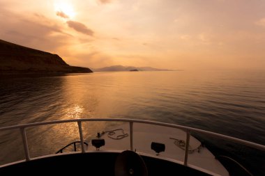 Tekneden gün batımına kadar görüntü. Turuncu gün ışığında suyun üzerinde yat. Van Gölü, Doğu Türkiye. Akdamar adasına gemi nakli. Dağ siluetleriyle çevrili deniz manzarası