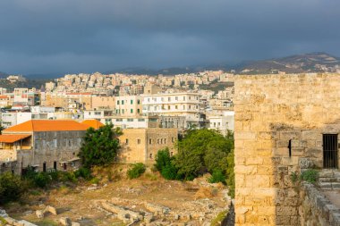 Byblos Haçlı Kalesi, Lübnan. Eski taş duvarların panoramik manzarası ve tepelerdeki Jbeil şehrinin modern manzarası. Şehrin tarihi ve modern kısımları
