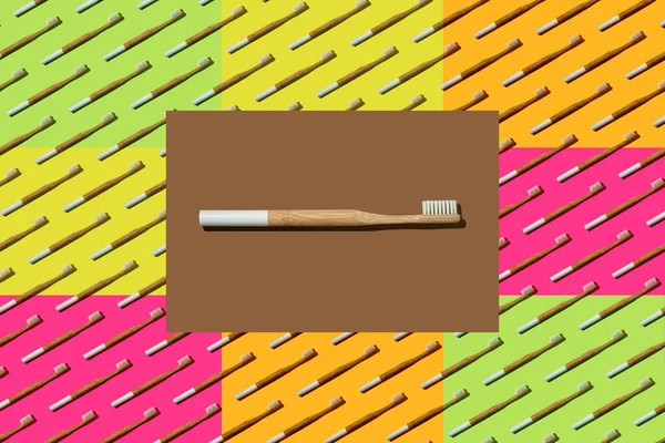 Bamboo toothbrush with a white bristles in brown rectangle on multicolor toothbrushes pattern