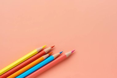 Pembe pastel arka planda renkli kalemler, düz uzanış. İşlenmemiş gökkuşağı kalemleri, kopyalama alanı. Kalemler sol alt köşede çapraz yatar..