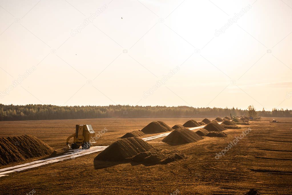 Turf extraction field with excavator tractor in sunset time, peat field