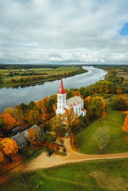 Sonbahar mevsiminde orman üzerindeki hava manzarası, nehir kenarındaki beyaz kilise. 