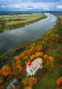 Sonbahar mevsiminde orman üzerindeki hava manzarası, nehir kenarındaki beyaz kilise. 