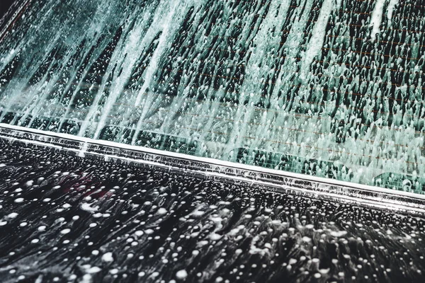 Car covered in white foam during cleaning, carwash washing process, car in soup