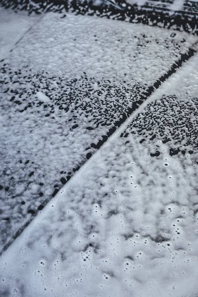 Car covered in white foam during cleaning, carwash washing process, car in soup