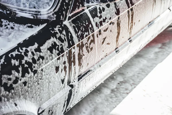 Car covered in white foam during cleaning, carwash washing process, car in soup