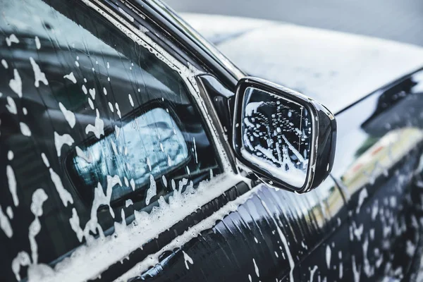 Car covered in white foam during cleaning, carwash washing process, car in soup