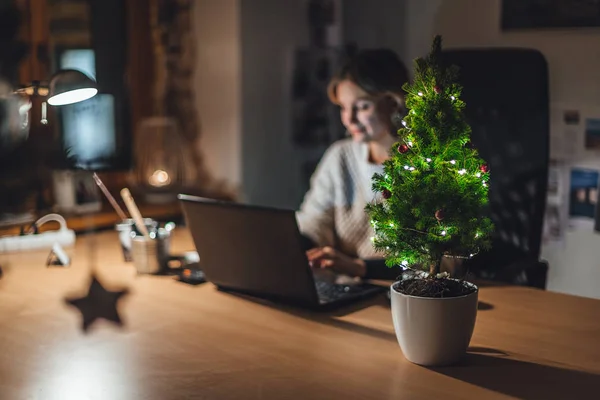 Ofiste süslenmiş Noel ağacı, bulanık arka planda iş kadını dizüstü bilgisayarla çalışıyor.