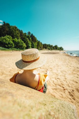Kumsalda güneşlenmekten hoşlanan kadınlar şapka takıyor. 