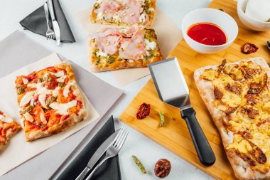 Soslu ve mutfak aletli farklı kare şekilli pizza dilimlerinin üst görüntüsü. İtalyan yemek masası 