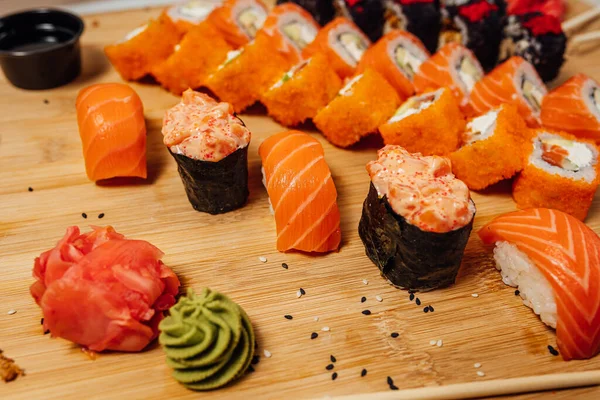 不同类型的寿司卷与生姜 芥末和筷子放在木板上 寿司放在桌上 — 图库照片