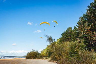 Açık mavi gökyüzüne karşı parlak sarı paraşütü olan bir paraglider.