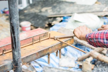 İnşaatçının elleri inşaat alanındaki demiri büküyor.