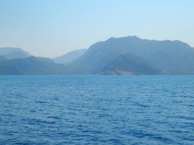 Deniz kenarındaki dağlar, sıradağlar ve kayalar, deniz manzaraları, mavi gökyüzü.