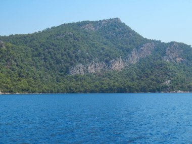 Deniz kenarındaki dağlar, sıradağlar ve kayalar, deniz manzaraları, mavi gökyüzü.