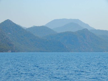 Deniz kenarındaki dağlar, sıradağlar ve kayalar, deniz manzaraları, mavi gökyüzü.