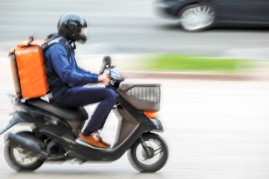 Maskeli iş adamları, yağmurlu bir günde şehir yolunda trafikte motosikletle teslimat yapıyor.