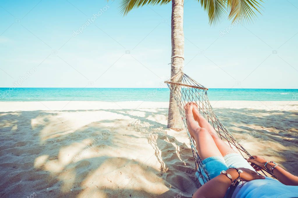 Leisure in summer - Beautiful Tanned legs of sexy women. relax and sunbathe on hammock at sandy tropical beach. vintage color styles