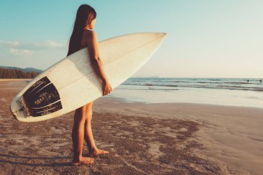 Bikinili sörfçü kadın sörf yapmaya gider. gün batımında sahilde sörf tahtası ile güzel seksi kadın. vintage renk ton