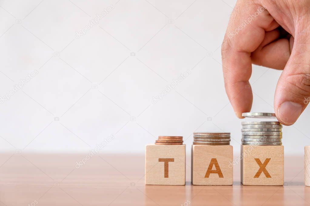 Concept of tax and financial management taxes season in business. Hand putting coins stack step staircase on wooden cube block with  TAX word. 