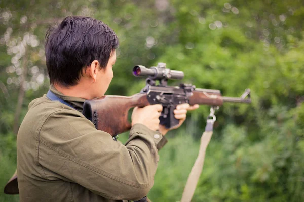 Hunter with a gun stands with his back against the background of the forest. The concept of a successful hunt, an experienced hunter. Hunting the summer season. The hunter has a large-caliber rifle and a hunting uniform. Image.