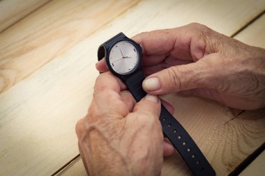 Yaşlı bir adamın elleri kol saatini tutuyor. Zamanın hızı kavramı, zamanın geçiciliği, yaşlılık. Görüntü.