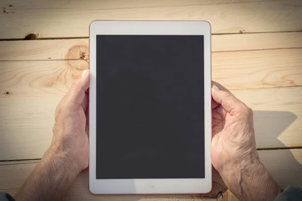 Hands of an elderly man are holding and using a tablet. The concept of teaching new technologies to older people, communication with the older generation, Internet access. Image.