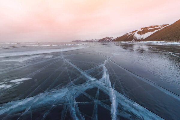 Baikal in the winter. The sky is burning in the rays of sunset. Cracks diverge in different directions.