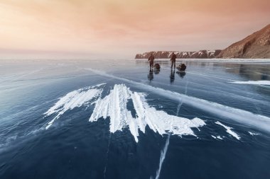 Baykal kışın iki gezginler günbatımında buz üzerinde git. Rusya, Sibirya.