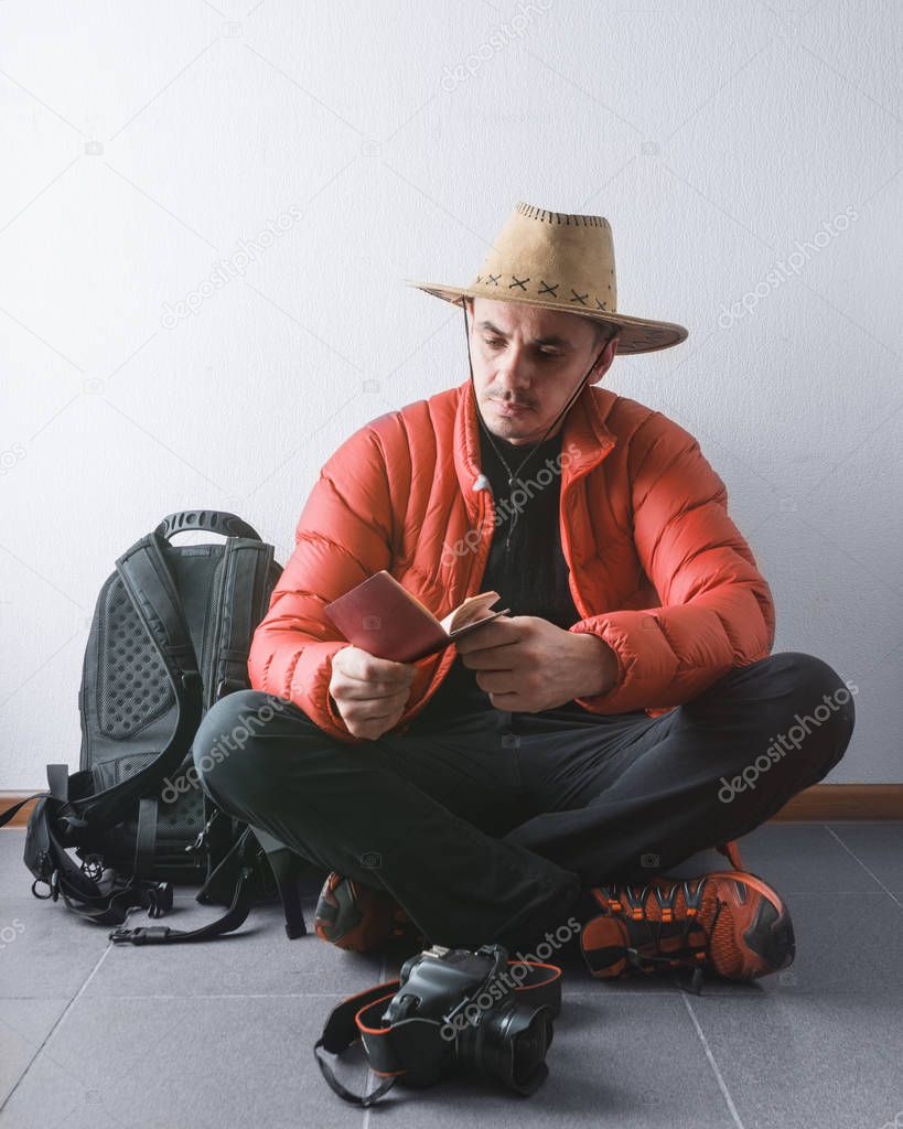 Travel concept. Tourist sits on the floor and looks into the passport. Near the backpack and camera. In a hat and coral jacket.