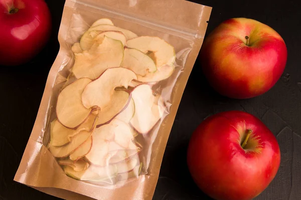 Apple fruit chips next to a fresh apple on a black background