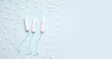 Regl sırasında tedavi kavramı can yakar. Mavi arka planda tamponların yanında haplar. Pankart