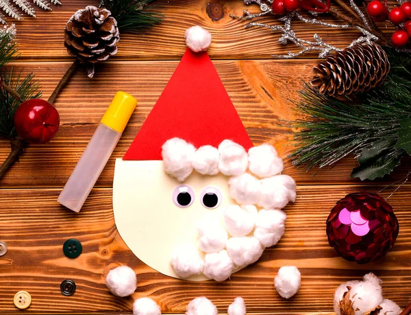 Adım adım Noel kartı yaz. Ahşap bir masadaki renkli kağıt ve pamuktan. Üçüncü adım.