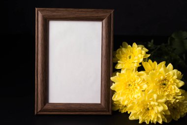 Siyah arkaplanda, sarı bir kasımpatının yanında duran bir fotoğraf için ahşap çerçeve. Boşluğu kopyala