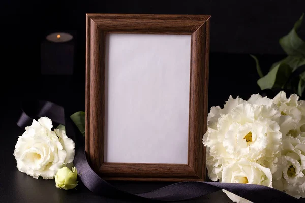 Siyah arkaplanda beyaz çiçeklerin yanında ahşap yas fotoğrafı çerçevesi
