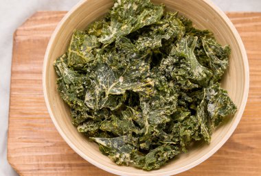 Ahşap bir tahtanın üzerindeki bir kasede lahana cipsi.