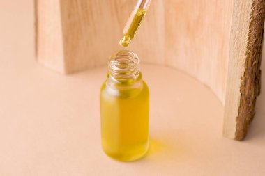 Organik yağlar konsepti. Ağaç dokusunun yanında damlatan bir şişe. Bej arkaplan